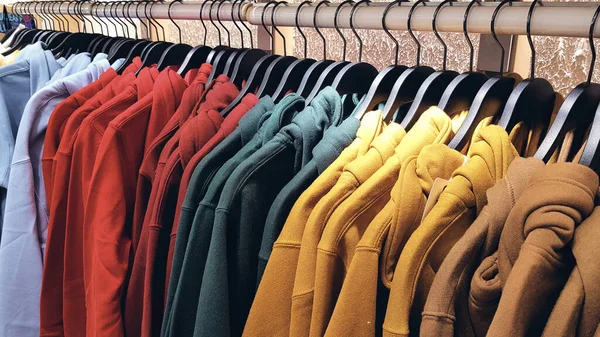 Sudaderas de colores brillantes colgando en una tienda de moda. Primer plano de multicolor amarillo, rojo, rosa, geen sudaderas cuelgan en una fila en una percha en la tienda de ropa en el centro comercial. — Foto de Stock