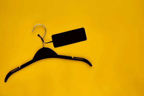 Black Coat hanger with black paper label isolated on yellow paper background. Clothing tag, label blank mockup template, to place your design. Black friday final sale banner.