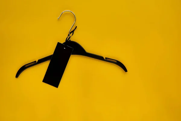 Black Coat hanger with black paper label isolated on yellow paper background. Clothing tag, label blank mockup template, to place your design. Black friday final sale banner.