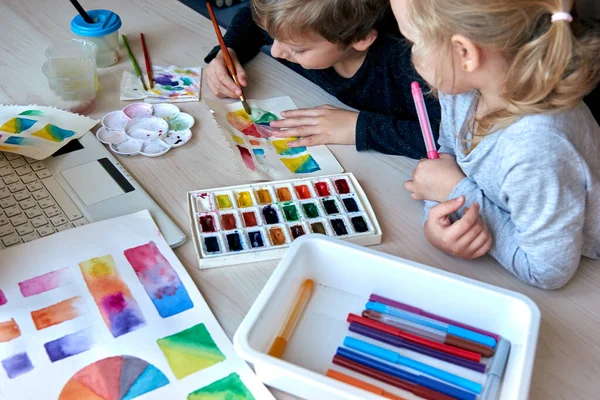 Children painting pictures with watercolor paints during art lesson. Pupils are concentrating on drawing with brush. Watercolor color wheel and palette. Color theory beginner hobby lessons.