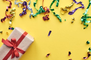 Noel kompozisyonu. Kırmızı kurdeleli bir hediye ve pastel kağıtlı renkli arka planda konfeti süslemeleri. Noel, kış, yeni yıl kutlama konsepti. Düz konum, üst görünüm, kopyalama alanı.