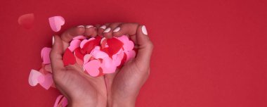 Sevgililer Günü kompozisyonu. Kırmızı arka planda pembe konfeti kalpleri tutan kadını kapat.