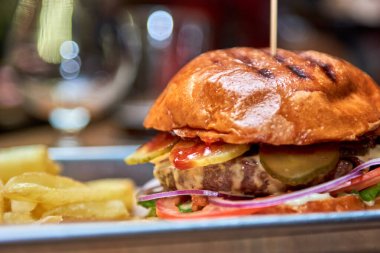 Lezzetli ev yapımı ızgara burger sığır eti, peynir, domuz pastırması ve ahşap masada fotokopi alanı ile sos. Patates kızartması ve birayla hamburger tutan eller. Bir grup arkadaş fast food yiyor.