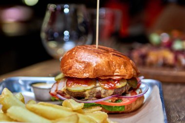Lezzetli ev yapımı ızgara burger sığır eti, peynir, domuz pastırması ve ahşap masada fotokopi alanı ile sos. Patates kızartması ve birayla hamburger tutan eller. Bir grup arkadaş fast food yiyor.