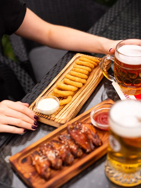 Assorted beer snacks, fast food. Bbq wings and Onion rings appetizer, cured cheese, meats, pickles, french fries, nachos, pistachios, chips and sauses with mug of beer.