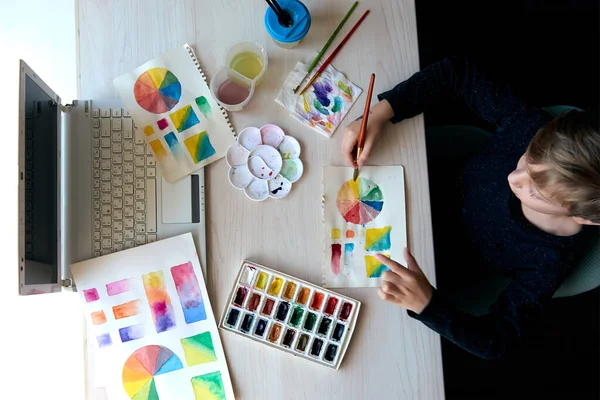 Boy painting pictures with watercolor paints during art lesson online — Stock Photo, Image