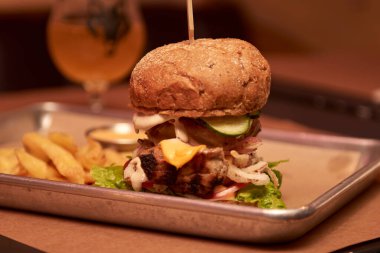 Lezzetli ızgara burger, biftek, peynir, pastırma ve sosla ahşap masada patates kızartması ve bira.
