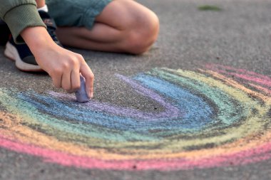 Çocuklar açık havada resim yapar. Çocuk asfalta gökkuşağı renginde tebeşir çiziyor.