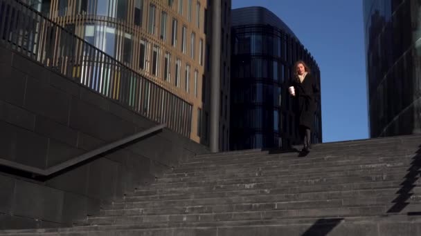Young business woman with coffee in hands runs down the stairs — Stok video