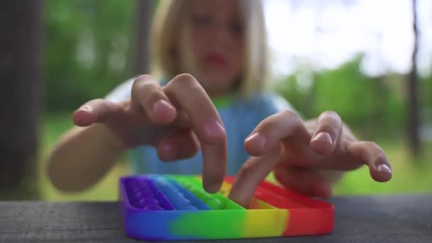Blonďatý chlapec sedí u stolu a hraje popit Rainbow Colors. — Stock video