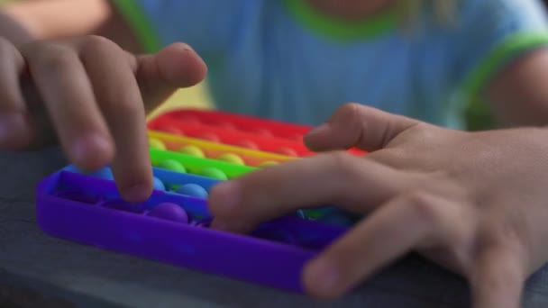 Rubia chico sentado en el parque y juega popit arco iris colores. — Vídeo de stock