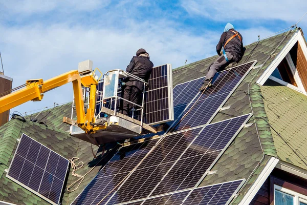 Workers installing solar panels on private home hexagonal roof felt on sunny day, blue sky. Real life. Home power plant.