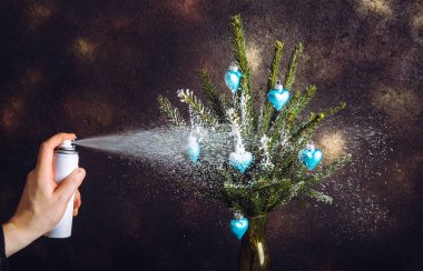 Kışın Noel ağacı dallarını spreylemek için sprey karla sprey sıkılmış insan eli görüntüsünü kapat, Art. Stüdyo ışıklarıyla çekilen karanlık arka plan..