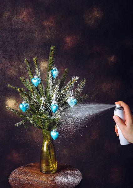 冬のクリスマスツリーの枝 芸術を飾るスプレーするために缶スプレー雪を使用して人の手のビューを閉じます スタジオライト室内暗い黒の背景で撮影 — ストック写真