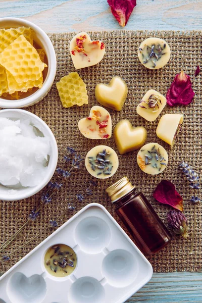 Making of mini wax melts for aroma lamp diffuser at home concept. Tools ingredients on table unbleached beeswax, solid coconut oil, essential oil, dried flowers and plastic mold. Flat lay view.