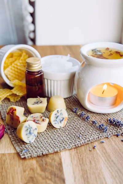 Ev yapımı mini mumları aromaterapi lambasında eritip ev içi konsept olarak kullanmak. Eriyen malzemeler, ağartılmamış balmumu, katı hindistan cevizi yağı, temel yağ, kurumuş çiçekler için masada malzemeler yapıyor..
