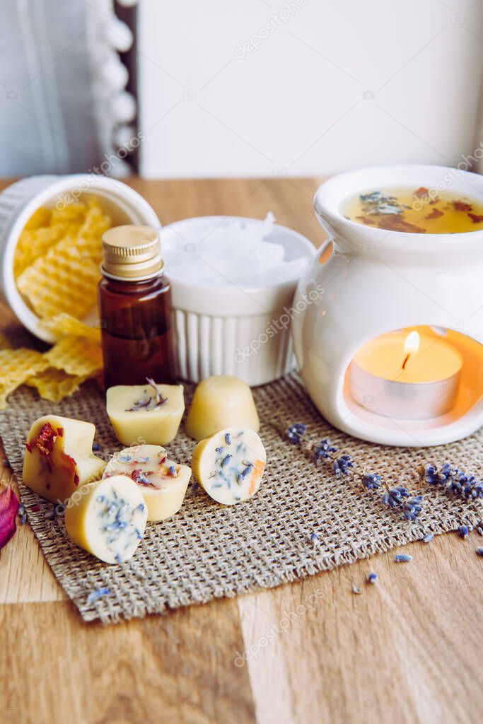 Using homemade mini wax melts in aromatherapy lamp diffuser at home interior concept. Melts making ingredients on table for unbleached beeswax, solid coconut oil, essential oil, dried flowers.
