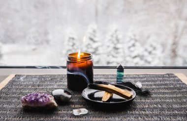 Palo Santo ahşabı, yağlı aromalı kutsal odun çubukları olarak bilinir. Negatif enerji konseptini temizleyen pencere pervazında yanan bir tabakta. Arka plandaki güzel kış manzarası kopya alanı ile bulanıklaştırılmış.