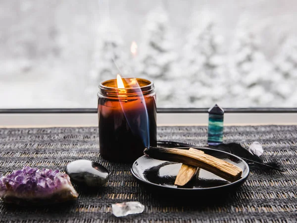 Palo Santo wood known as oily aromatic holy wood sticks smouldering on plate on home window sill cleaning negative energy concept. Beautiful winter landscape on background blurred with copy space.