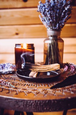 Palo Santo ahşabı, yağlı aromalı kutsal odun çubukları olarak bilinir, oturma odasında yanan tabakta negatif enerji kavramını temizler. Bohem tarzı kır evi dekorasyonu.