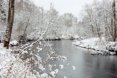 Taze karla kaplı ağaçlarla çevrili, kışın akan nehir suyunun uzun kepenk fotografı. Estonya 'daki Keila Nehri.
