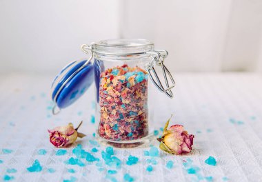 Ev yapımı kuru gül yaprakları çiçek banyosu aromaterapi için tuz karışımı ve küvette rahatlama, banyo karışımı. Küçük şirin bir kavanozun içinde. Beyaz arka planda bitki ve çiçek yapraklarıyla karıştırılmış banyo tuzu.