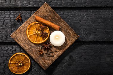 Kış baharatları konsepti. Çeşitli baharatların düz görünümü: tarçın çubuğu, karanfil, yıldız anason, kurutulmuş portakal dilimleri. Mevsimlik ahşap kaplama, dramatik siyah yanmış ahşap arka plan..