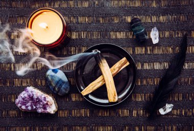 Palo Santo tahtası, yağlı aromalı kutsal odun çubukları olarak bilinen ev masasında yanan ve negatif enerji kavramını temizleyen tabakta yatıyordu. Etrafı ametist ve labradorit taşlarıyla çevrili..