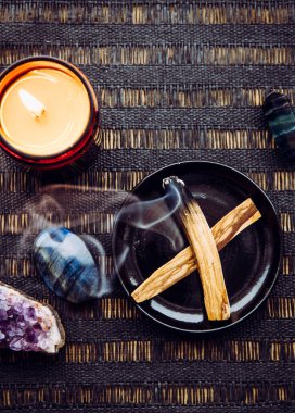 Palo Santo tahtası, yağlı aromalı kutsal odun çubukları olarak bilinen ev masasında yanan ve negatif enerji kavramını temizleyen tabakta yatıyordu. Etrafı ametist ve labradorit taşlarıyla çevrili..