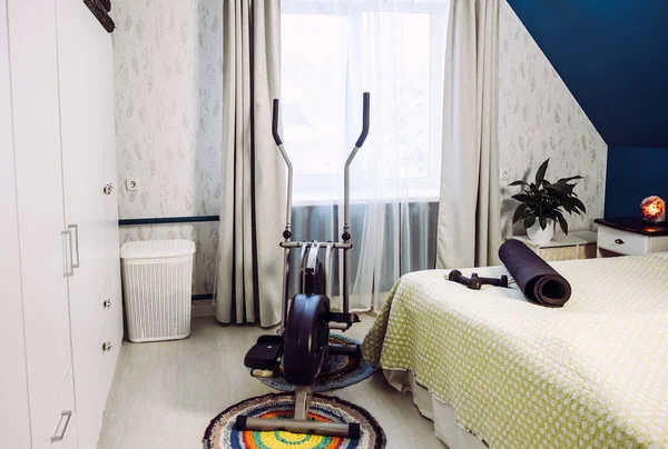 Elliptical trainer, weights, yoga mat at home gym located in bedroom.