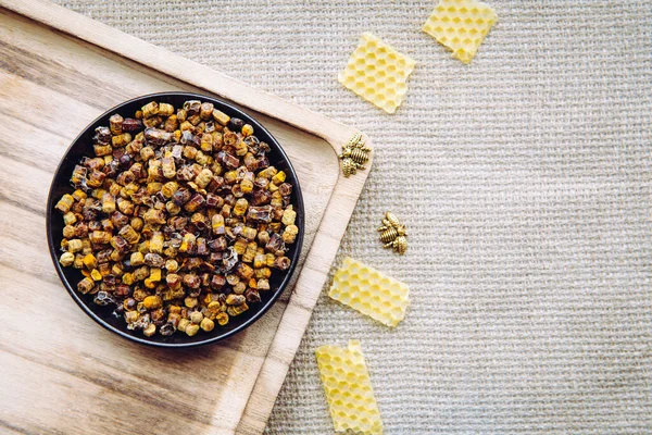 Alternative medicine bee bread ( fermented flower and plant pollen by honey bees) pellets on plate. Beeswax cera alba and bee figurines for decoration vintage jute cloth.