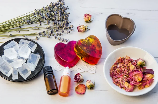 Making handmade soap with crystal clear melt and pour soap mixture. Ready to use pink and yellow tied soaps with rose petals and lavender blossoms in center surrounded by ingredients.