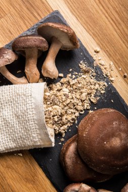 Siitake mantarından yapılmış kuru toz, Lentinula edodes. Ahşap zemin üzerinde taze şitake mantarlarıyla siyah taş kesme tahtasındaki besin maddeleri..