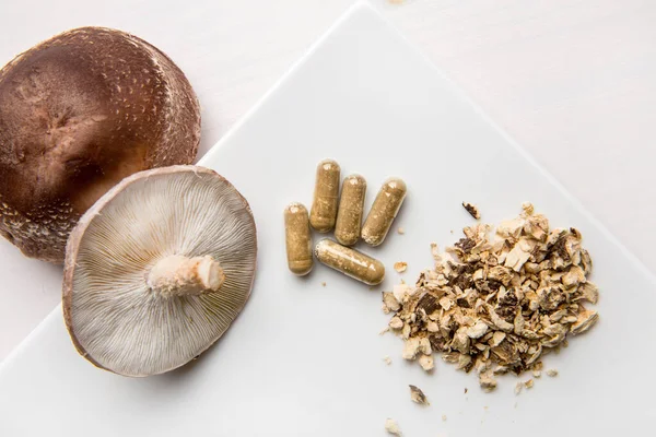 Shiitake Lentinus edoides mantar takviyesi kapsülleri taze Shiitake mantarları ve beyaz arka planda pudralanmış. Düz görünüm.