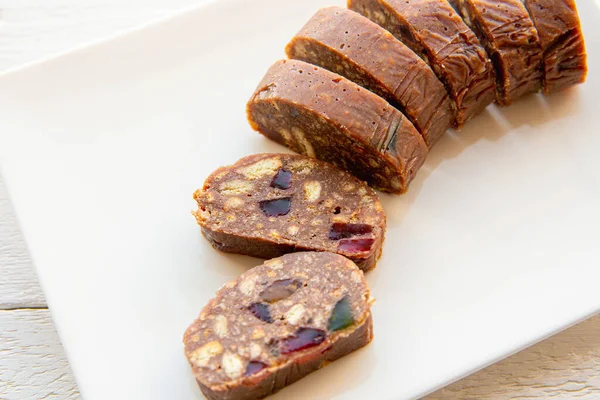 Homemade Estonia local cake called: Spotted Dog. Made with cookies, marmalade, cacao and butter. Local Estonian cuisine concept. Above view of sliced cake on white plate and wooden background.