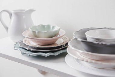 Mutfak rafında temiz, değişik şekillerde ve renkli, antika tabak yığınları var. Pastel renk, beyaz minimal arkaplan.