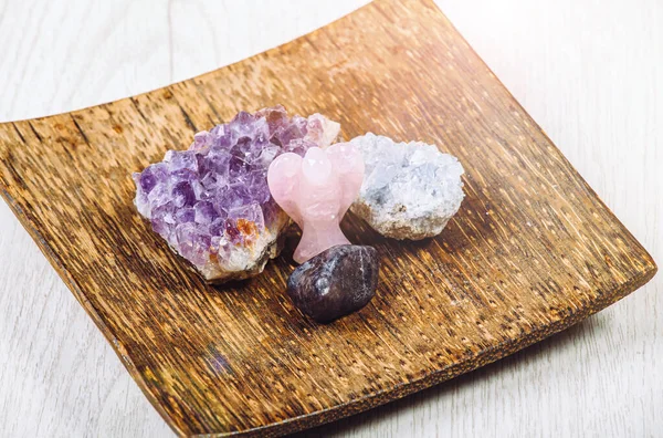 Group of gemstones on wooden tray in home interior. Rose quarz angel figurine, amethyst geode and celestite geode cluster and iolite cordierite or steinheilite.