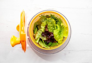İçinde yapraklı yeşillikler olan salata karıştırıcı alet çanağının en üst görüntüsü. Salata yapraklarını kurutmak ve yıkamak için rahat bir yol..