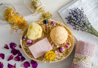 Güzellik banyosu ürünlerinde kullanılan farklı doğal kurutulmuş bitkiler. Banyo bombasının üst görüntüsü, doğal deniz süngeri, bir kalıp sabun, aroma yağı şişesi ve etrafa saçılmış kuru otlarla dolu kavanozlar..