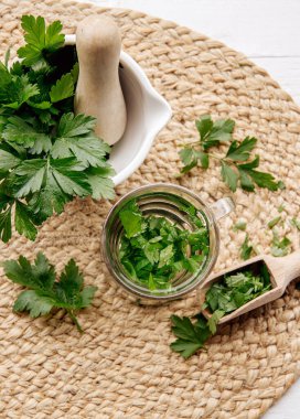 Maydanoz Petroselinum gevreğinden yapılan ev yapımı şifalı bitki çayının üstünde. Yeşil yapraklar çay fincanında beyaz ahşap zemin üzerinde taze havan ve tokmak yapraklarıyla.