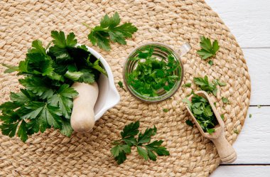 Maydanoz Petroselinum gevreğinden yapılan ev yapımı şifalı bitki çayının üstünde. Yeşil yapraklar çay fincanında beyaz ahşap zemin üzerinde taze havan ve tokmak yapraklarıyla.