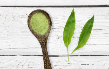 Ramson, Buckram, geniş yapraklı sarımsak, ahşap sarımsak, ayı pırasası ya da ayı sarımsağı olarak bilinen Allium ursinum yapraklarından ev yapımı yabani sarımsak tuzu. Tahta arka planda ağaç kaşık üzerinde bitki yaprakları ve bitkisel tuz.