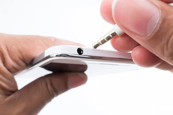 Mano sosteniendo el teléfono inteligente blanco y enchufando el cable del teléfono principal — Foto de Stock