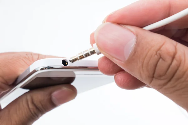 Mano sosteniendo el teléfono inteligente blanco y enchufando el cable del teléfono principal — Foto de Stock