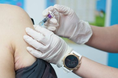 Doktorun yakın çekim görüntüsü. Aşı enjeksiyonu. Asyalı adamın omzuna kovid aşılama için.