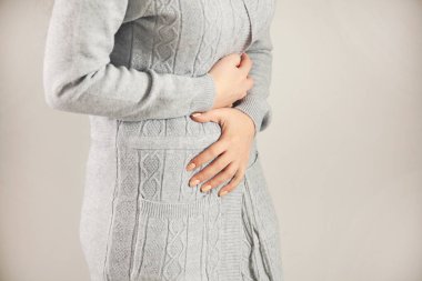 Gri arka planda karın ağrısı çeken bir kadın.