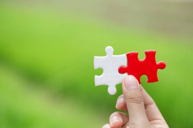 Bir işadamının elinde kırmızı bir yapboz var. Yeşil doğal arka plan iş konsepti organizasyon işbirliği Eksik parçaların seçimi Başarı ve sembolik bağlantı stratejileri.