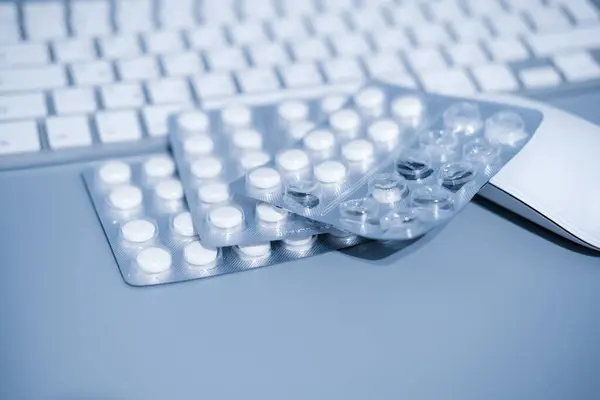 White keyboard and blistered pills on blue background. Work and health concept