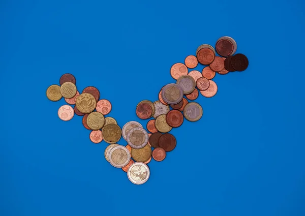 Coins in form of tick mark on blue background. Top view