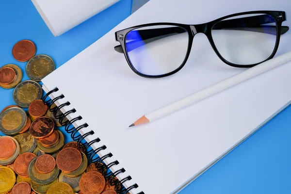 Finans planlaması ve ekonomi konsepti. Mavi arkaplanda defter, kalem, gözlük ve bozukluklar